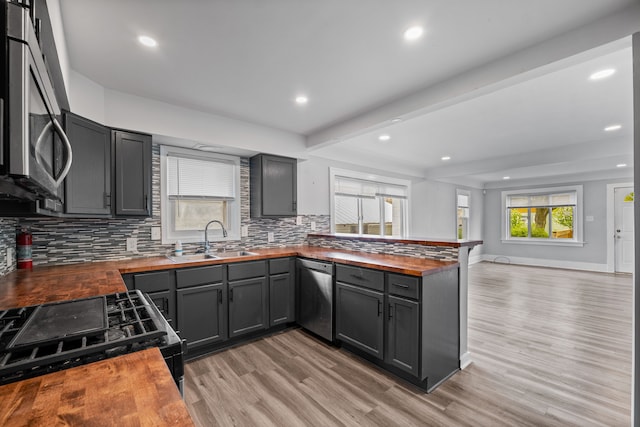 kitchen featuring butcher block counters, a sink, appliances with stainless steel finishes, open floor plan, and a peninsula