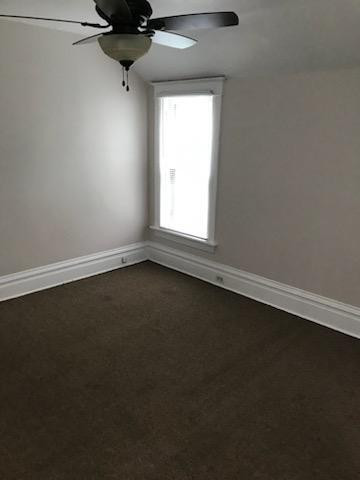 spare room with dark carpet, baseboards, and ceiling fan