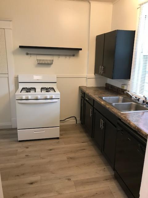kitchen featuring gas range gas stove, a sink, black dishwasher, light wood-type flooring, and dark countertops