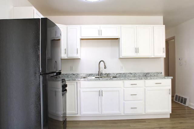kitchen featuring freestanding refrigerator, a sink, white cabinetry, light stone counters, and wood finished floors
