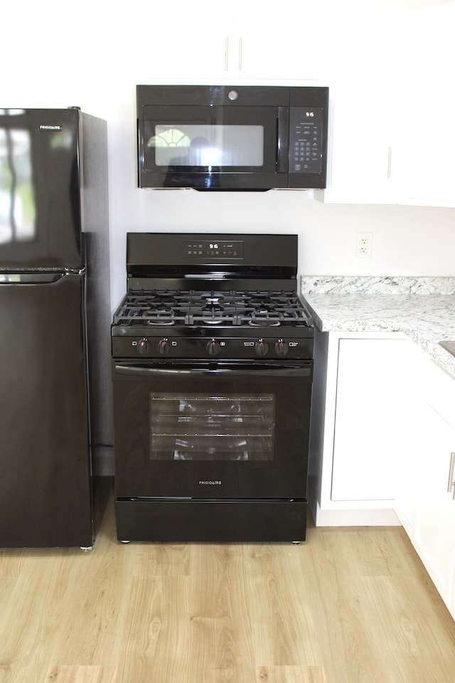 kitchen featuring black appliances, light wood-style floors, light stone countertops, and white cabinetry