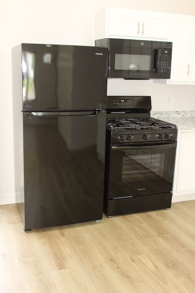 kitchen with black appliances, white cabinetry, light wood finished floors, and light stone countertops