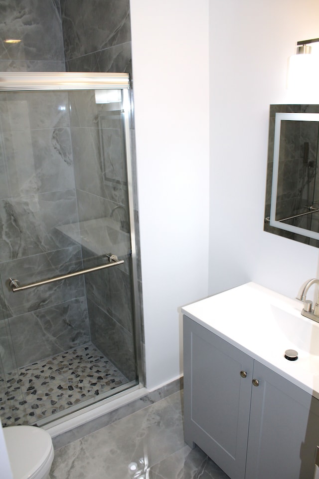 bathroom featuring a stall shower, toilet, vanity, and marble look tiles