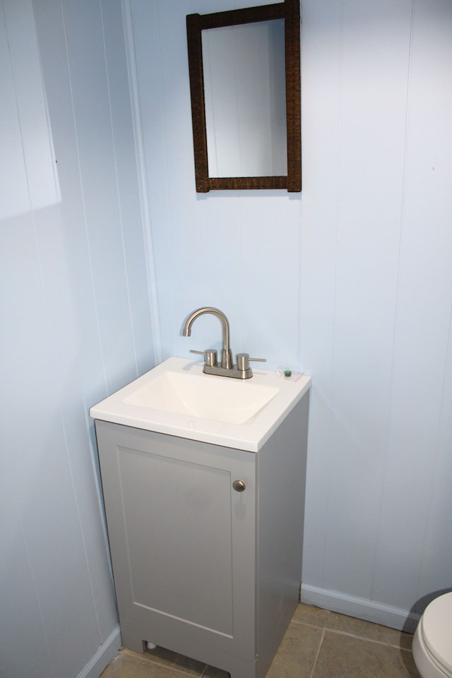 half bath featuring a decorative wall, vanity, baseboards, and toilet