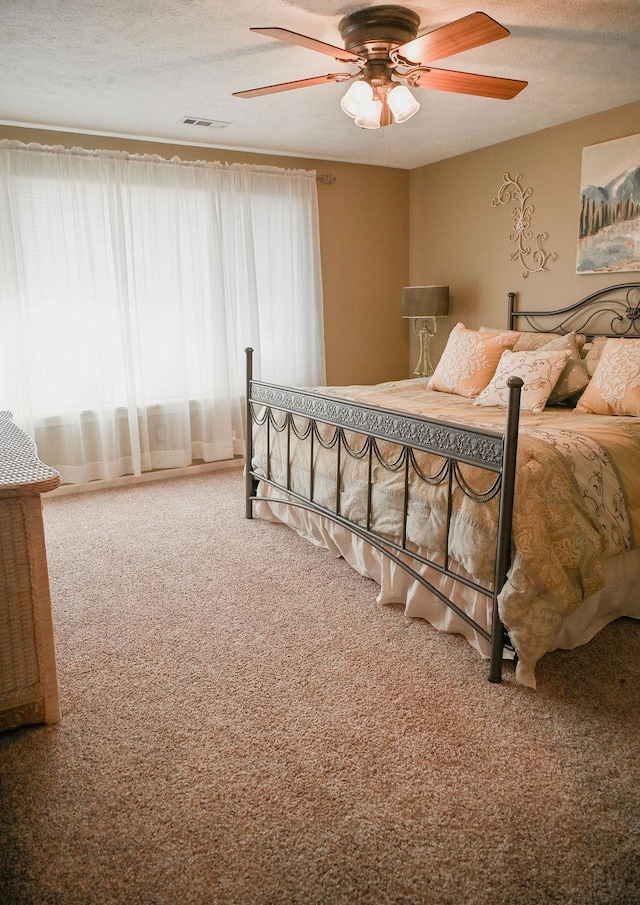 carpeted bedroom featuring a ceiling fan and a textured ceiling