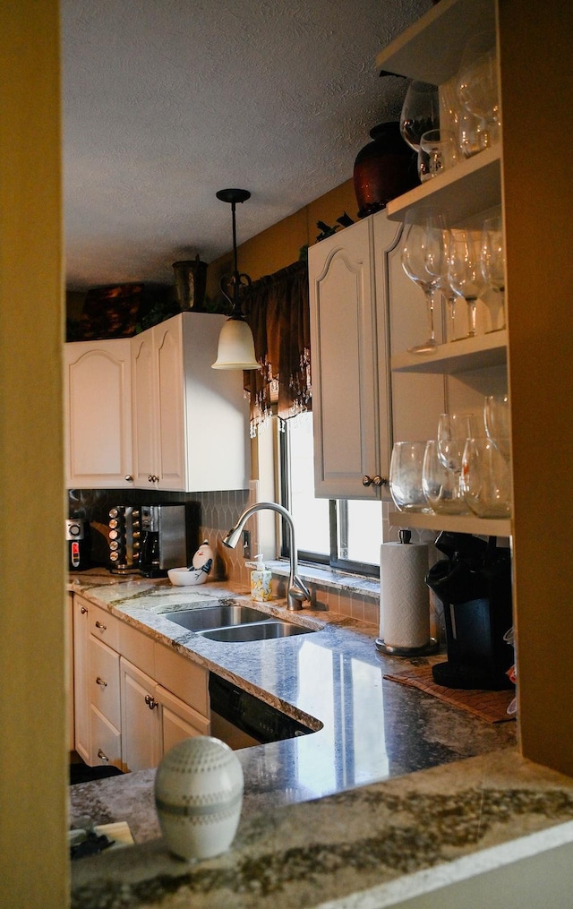kitchen with a sink, a textured ceiling, decorative backsplash, white cabinetry, and stone counters