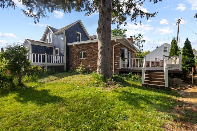 rear view of house with a wooden deck, brick siding, a chimney, and a yard