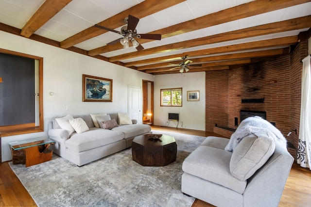 living room with wood finished floors, beam ceiling, a ceiling fan, and a brick fireplace