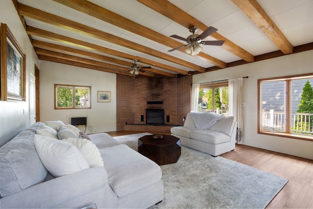 living area featuring ceiling fan, beam ceiling, a brick fireplace, and wood finished floors