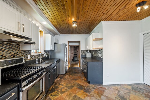 kitchen featuring appliances with stainless steel finishes, dark countertops, under cabinet range hood, crown molding, and a sink