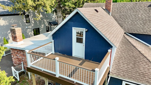 back of property with a shingled roof and a chimney