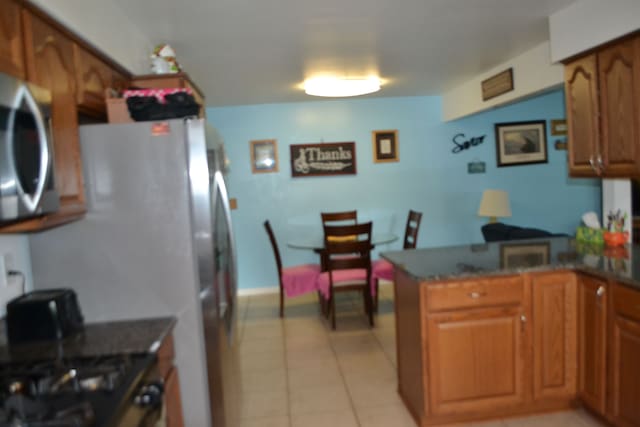 5448 Fairview Dr, Grand Blanc, MI 48439 - kitchen featuring brown cabinetry, stainless steel microwave, light tile patterned floors, a peninsula, and gas range