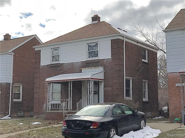 view of front of house with brick siding, a chimney, and covered porch
