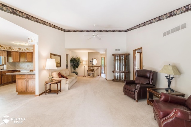 living room with light colored carpet, a towering ceiling, a ceiling fan, and baseboards