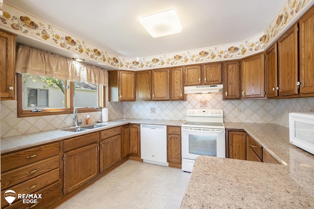 kitchen featuring white appliances, under cabinet range hood, a sink, and brown cabinetry