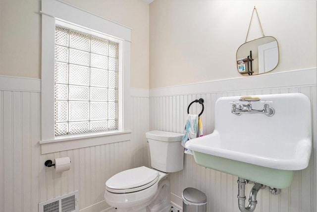 bathroom featuring a wainscoted wall, toilet, plenty of natural light, and a sink