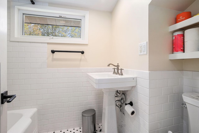 bathroom featuring tile walls, wainscoting, toilet, a bathtub, and a shower