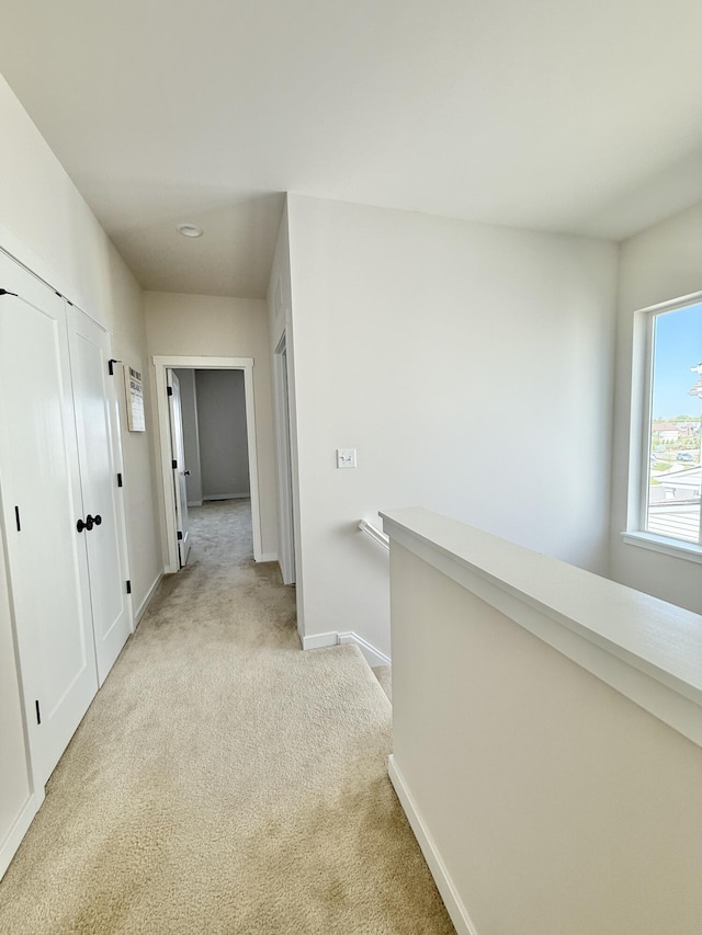 hall featuring light colored carpet, baseboards, and an upstairs landing
