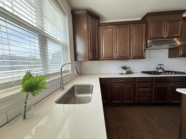 kitchen with a sink, under cabinet range hood, stainless steel gas stovetop, light countertops, and decorative backsplash