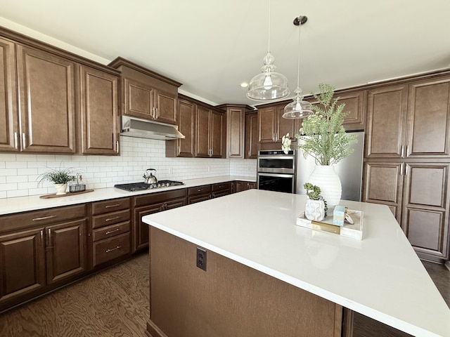 kitchen featuring stainless steel appliances, under cabinet range hood, light countertops, a kitchen island, and dark brown cabinetry