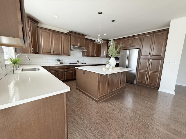 kitchen with a sink, stainless steel appliances, a center island, tasteful backsplash, and under cabinet range hood