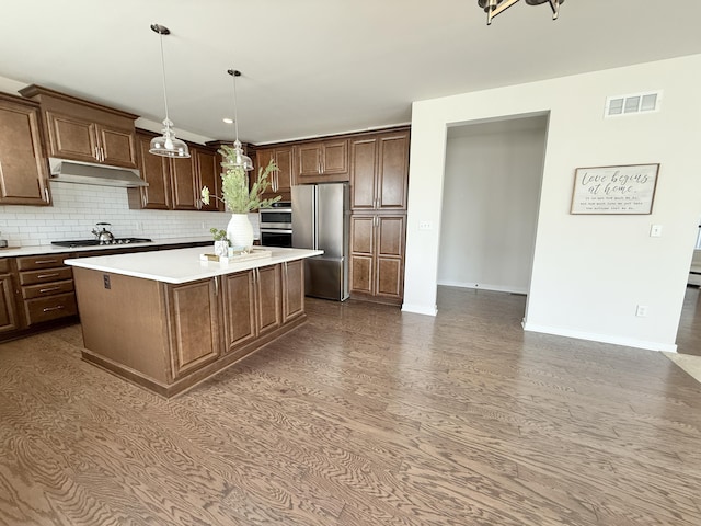 kitchen with freestanding refrigerator, gas cooktop, under cabinet range hood, light countertops, and backsplash