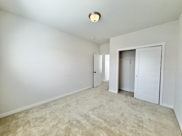 unfurnished bedroom featuring light colored carpet, a closet, and baseboards