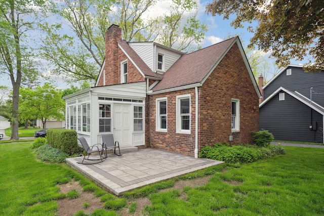 back of house featuring a patio, a chimney, brick siding, a yard, and roof with shingles
