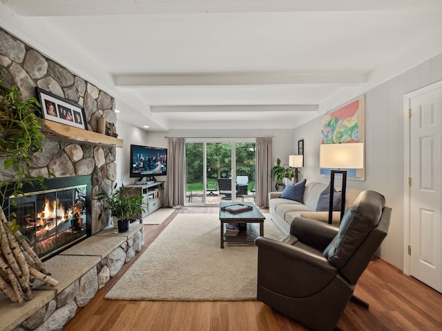 living room featuring a stone fireplace, beam ceiling, and wood finished floors