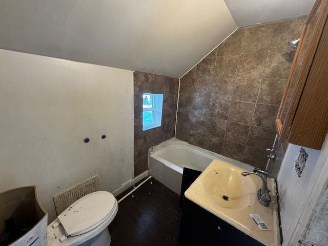 1143 Ballard St, Lansing, MI 48906 - full bathroom featuring vaulted ceiling, toilet, a tub to relax in, tile walls, and vanity