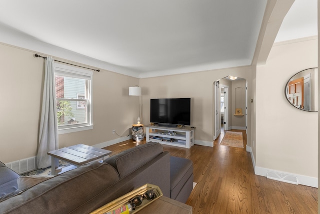 living room featuring arched walkways, wood finished floors, and baseboards