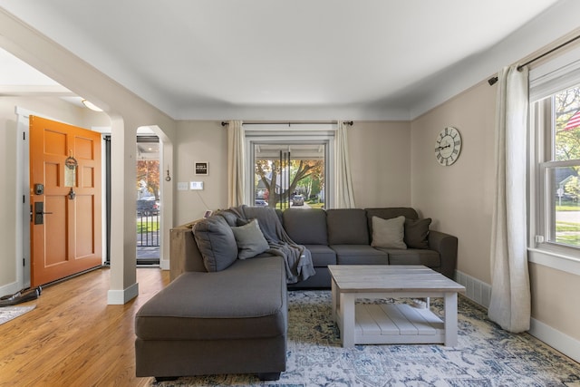 living area featuring arched walkways, healthy amount of natural light, baseboards, and light wood-style floors