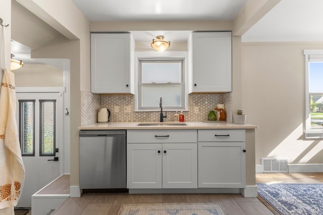 kitchen featuring stainless steel dishwasher, a sink, backsplash, light countertops, and white cabinetry