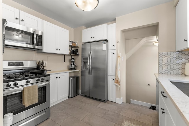 kitchen with stainless steel appliances, backsplash, white cabinets, and light stone counters