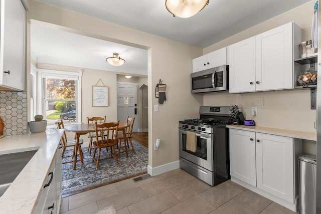 kitchen with stainless steel appliances, white cabinetry, decorative backsplash, light stone counters, and light tile patterned flooring