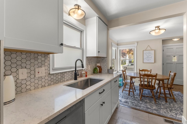 kitchen with a sink, stainless steel dishwasher, decorative backsplash, light stone counters, and white cabinetry