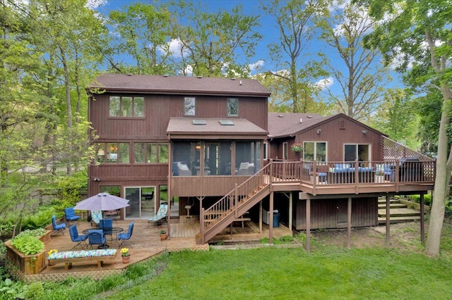 back of property with a sunroom, a deck, roof with shingles, stairs, and a lawn