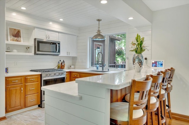 kitchen featuring stainless steel appliances, a peninsula, open shelves, a sink, and a breakfast bar area