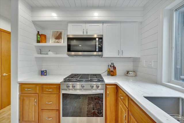 kitchen featuring stainless steel appliances, open shelves, light stone countertops, wood walls, and white cabinetry