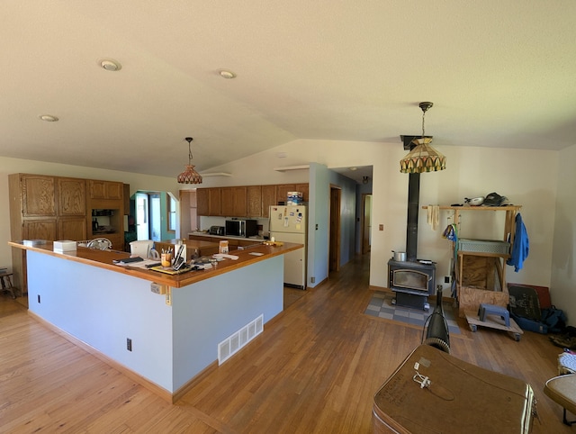 kitchen with freestanding refrigerator, light wood finished floors, brown cabinetry, lofted ceiling, and decorative light fixtures