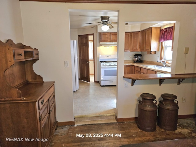 1551 Division St, Saginaw, MI 48602 - kitchen with white appliances, a sink, under cabinet range hood, a ceiling fan, and a breakfast bar area