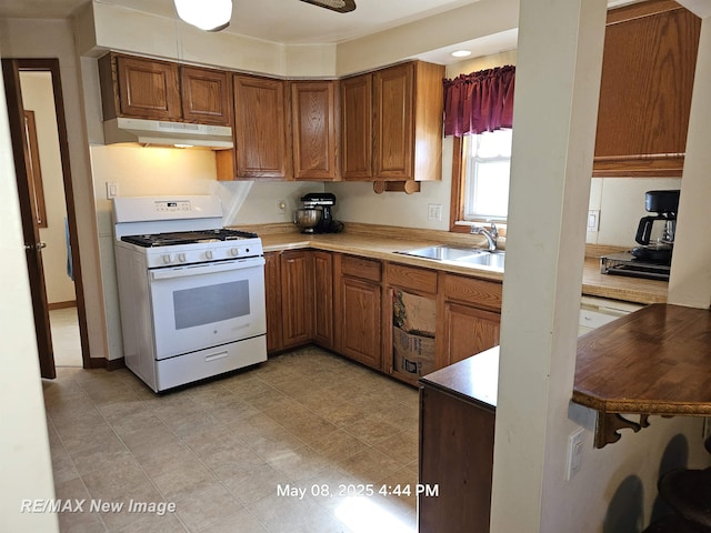 1551 Division St, Saginaw, MI 48602 - kitchen with white range with gas stovetop, under cabinet range hood, a sink, brown cabinets, and light countertops