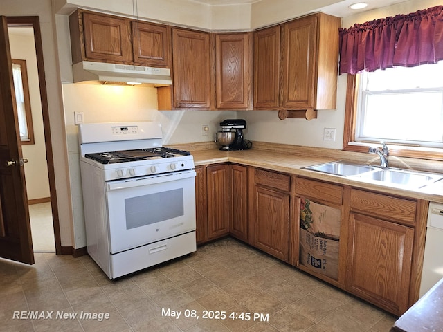 1551 Division St, Saginaw, MI 48602 - kitchen featuring white range with gas stovetop, under cabinet range hood, a sink, brown cabinets, and light countertops