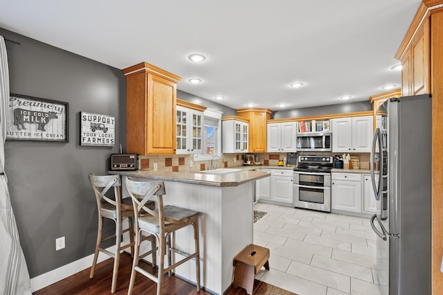 15974 Rustic Ln S, Vicksburg, MI 49097 - kitchen with appliances with stainless steel finishes, a peninsula, tasteful backsplash, glass insert cabinets, and recessed lighting