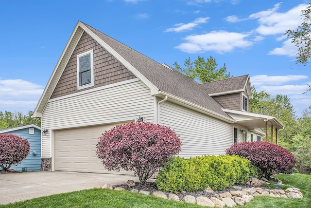 view of side of property with concrete driveway, roof with shingles, and an attached garage