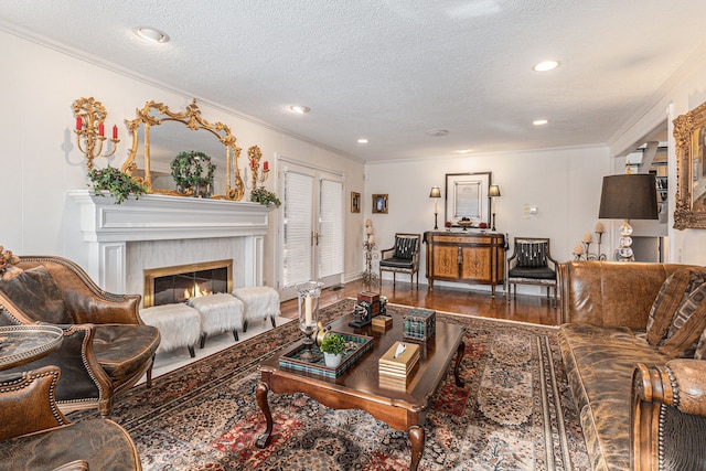 living area with crown molding, wood finished floors, a textured ceiling, a glass covered fireplace, and recessed lighting