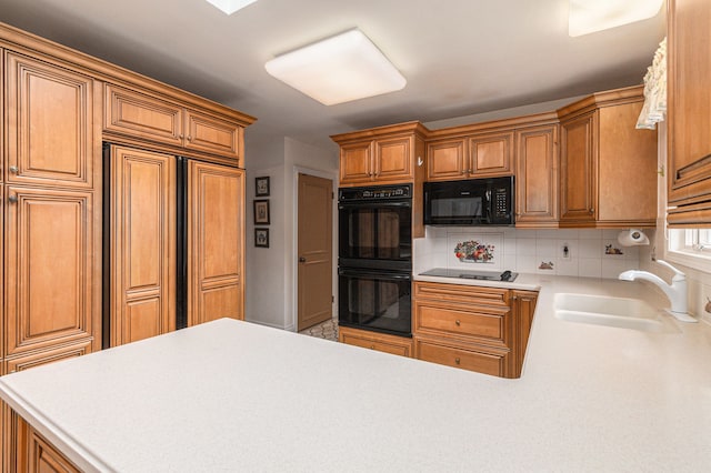 kitchen with black appliances, a sink, backsplash, a peninsula, and light countertops