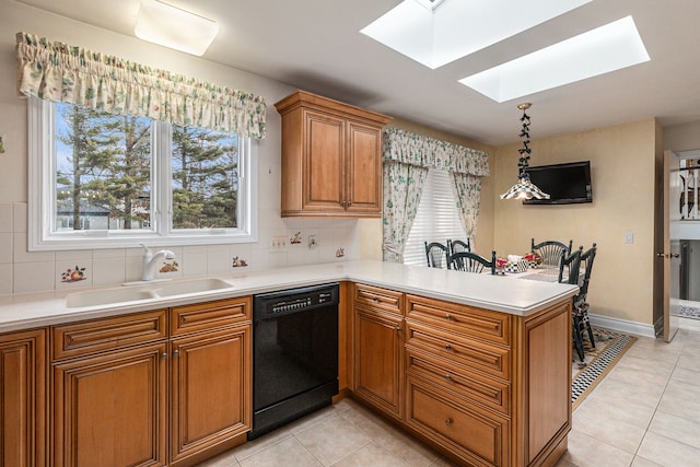 kitchen featuring dishwasher, a skylight, a sink, brown cabinetry, and a peninsula