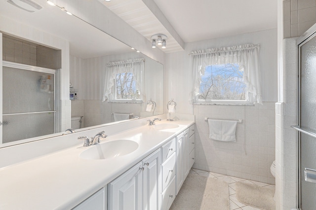 bathroom featuring toilet, tile walls, tile patterned flooring, a stall shower, and double vanity