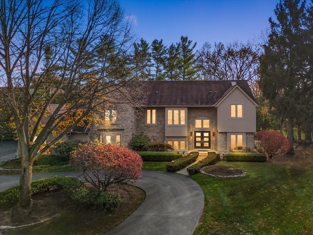 view of front of property with french doors, curved driveway, a yard, and stone siding